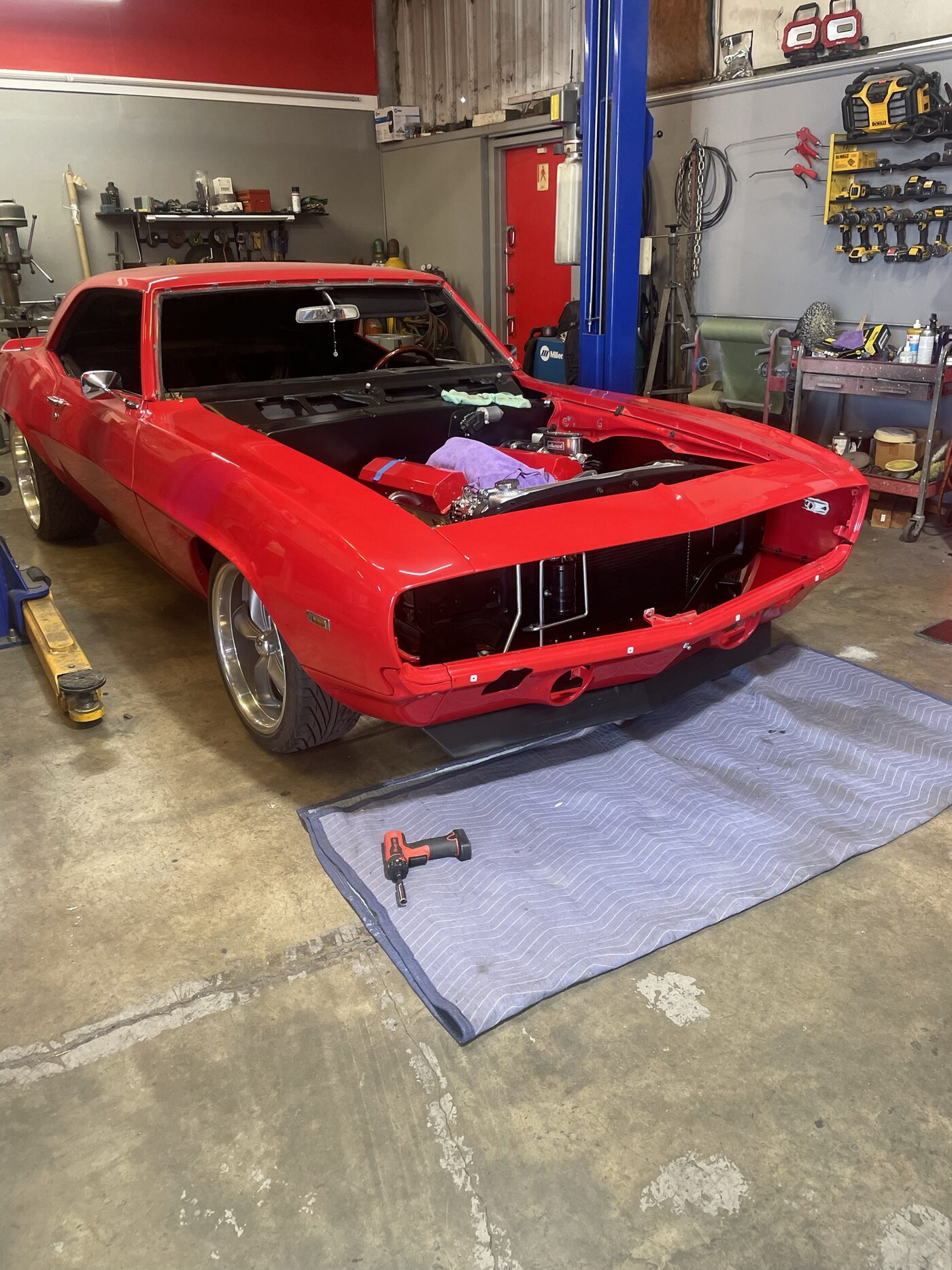 A red first generation Camaro with the windshield out, ready for new glass