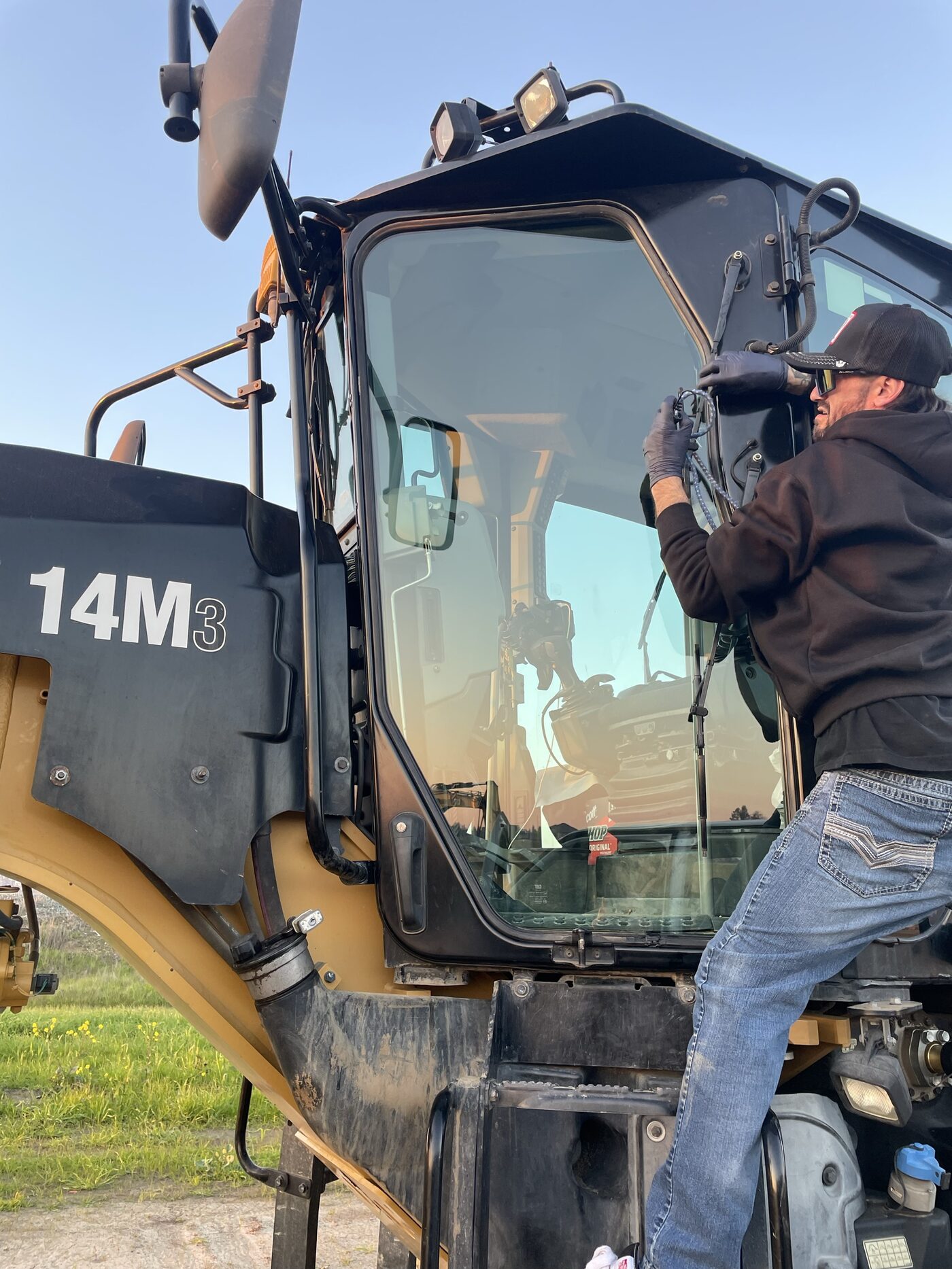 An Accurate Auto Glass technician installing cab glass on a Cat motor grader