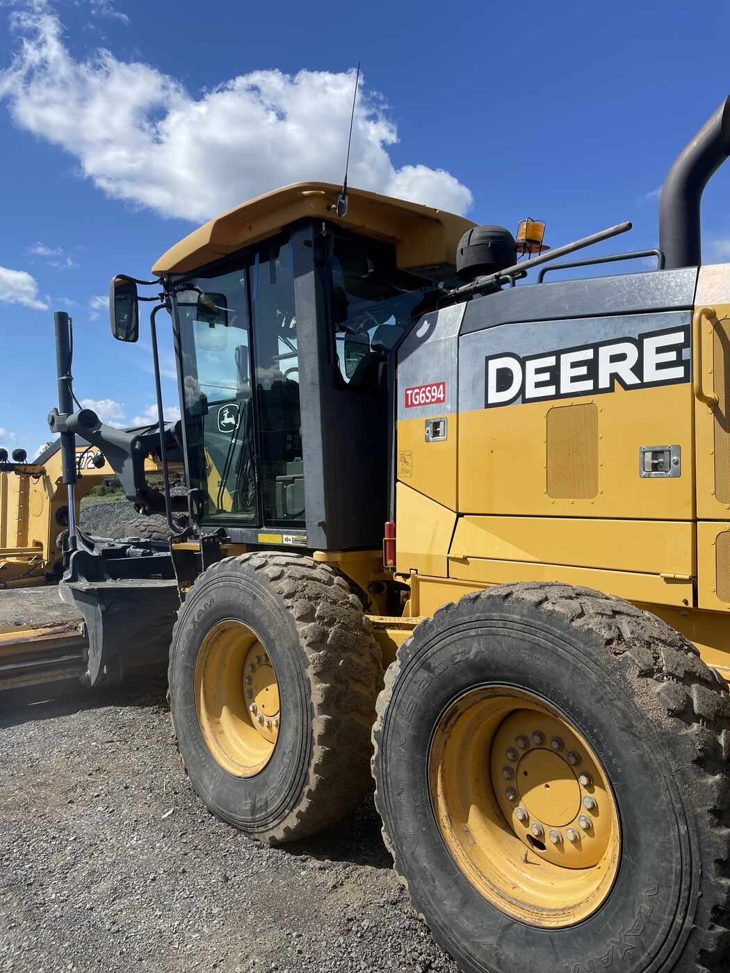 John Deere motor grader on a job site, cab glass replaced